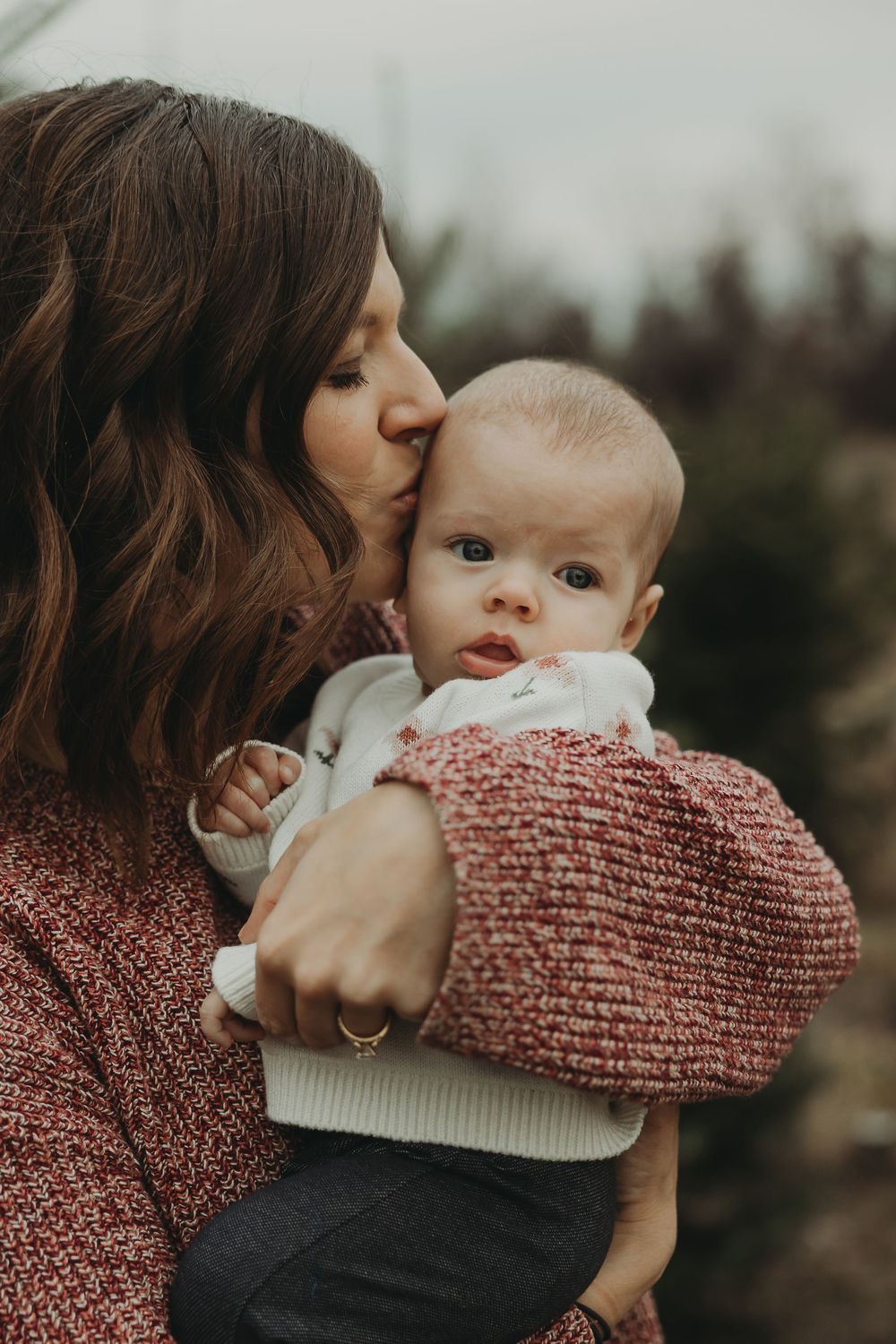 Tender outdoor portrait series showing intimate moments between parent and baby in warm winter clothing.
