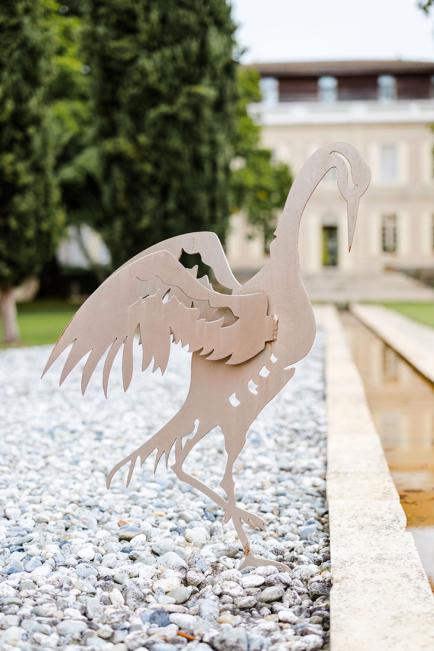 Metal silhouettes of roosters arranged in a row on a stone wall with white gravel below.