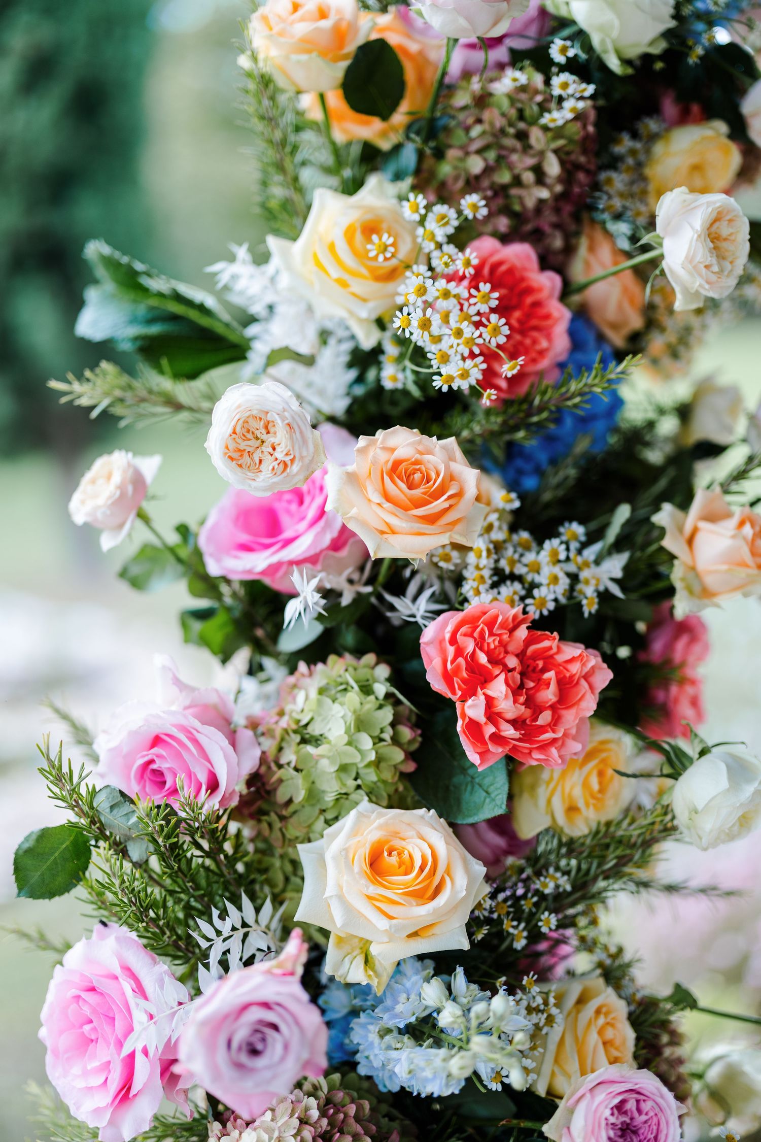 Beautiful floral arrangement with peach and pink roses, carnations, and delicate blue flowers mixed with greenery.
