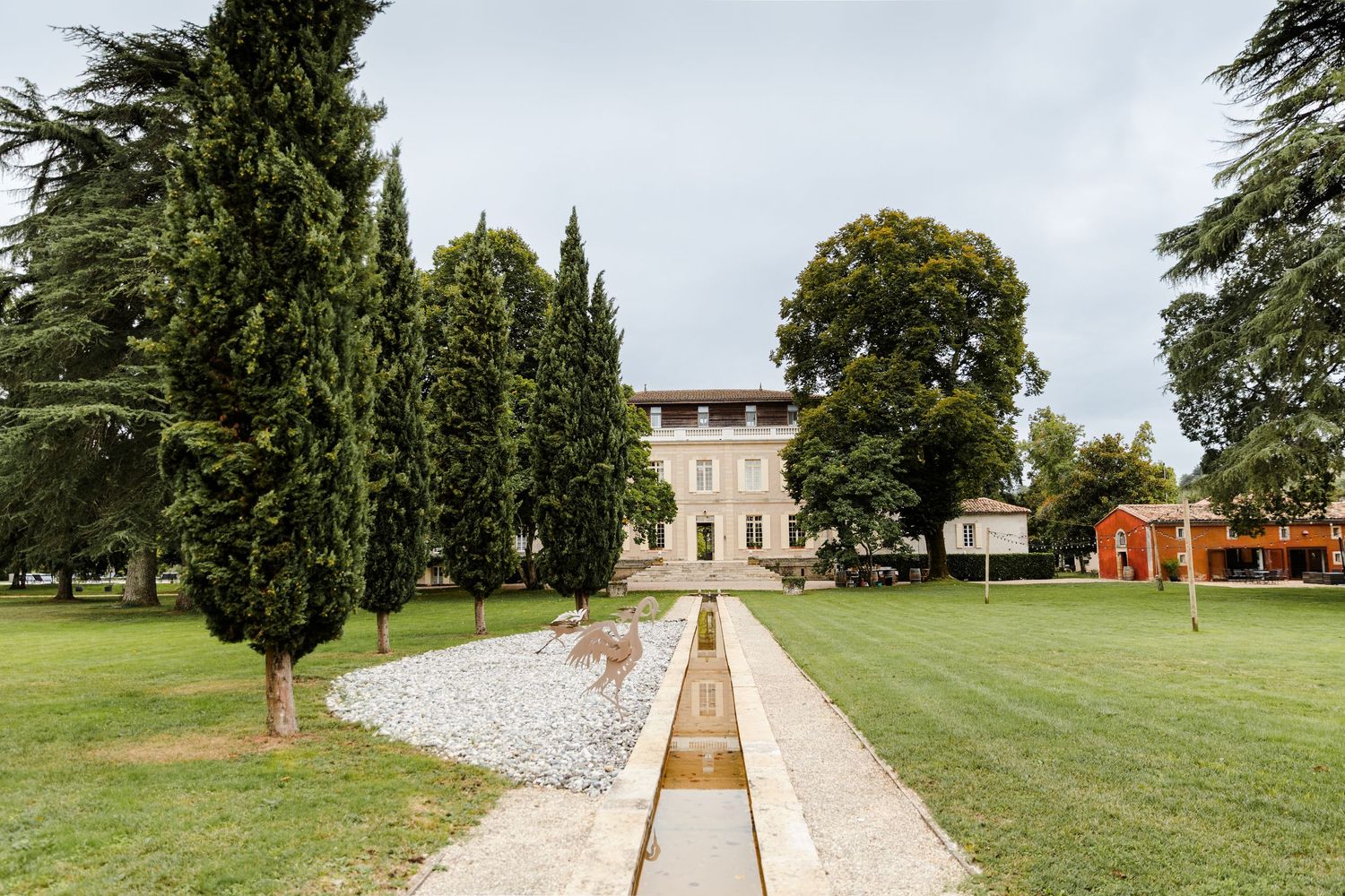 A scenic stone path leads through a green park towards a historic mansion building in the distance.