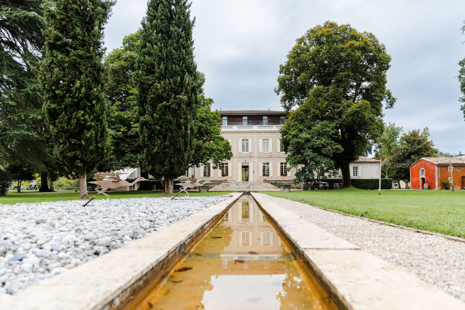 A long gravel pathway leads through a lush green park towards a stately historic building on a summer day.