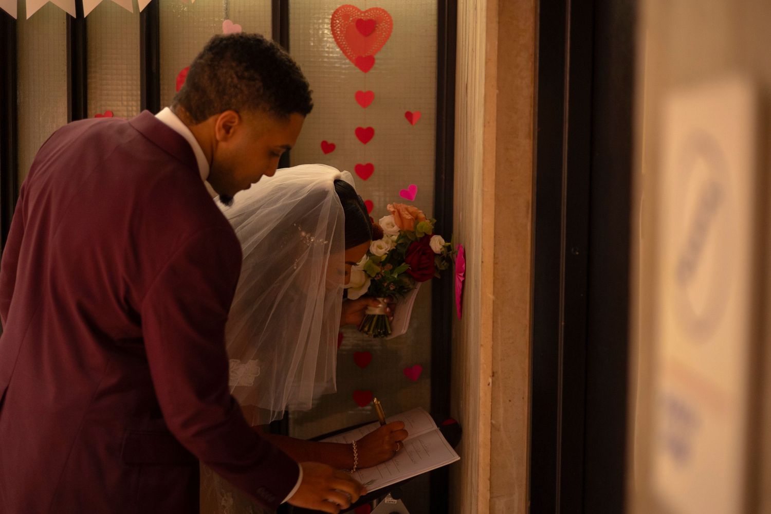 A couple shares a tender moment in a dimly lit hallway decorated with heart-shaped decorations.
