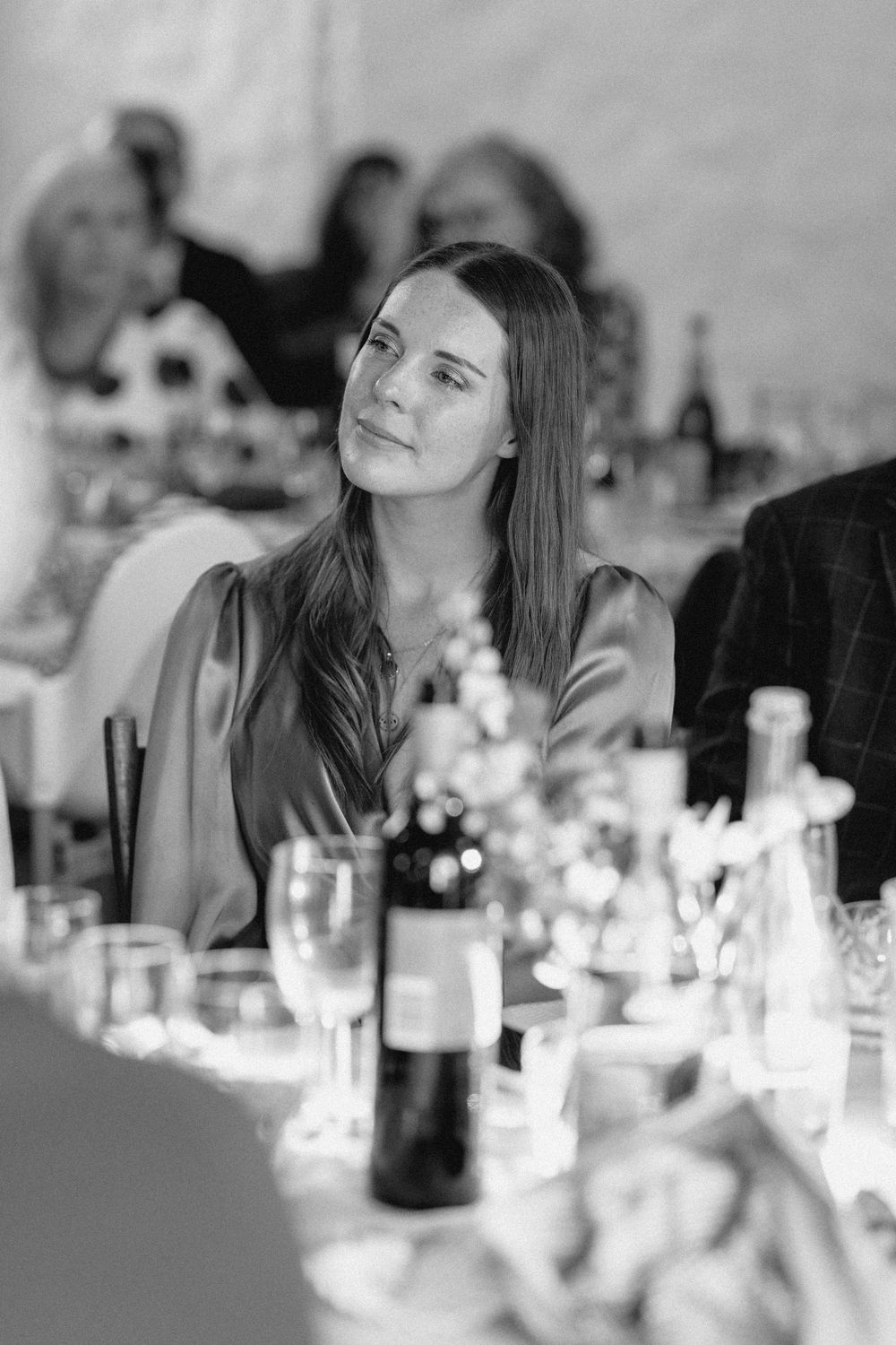 Black and white photo of a guest at an elegant dinner party with table settings and wine bottles visible.