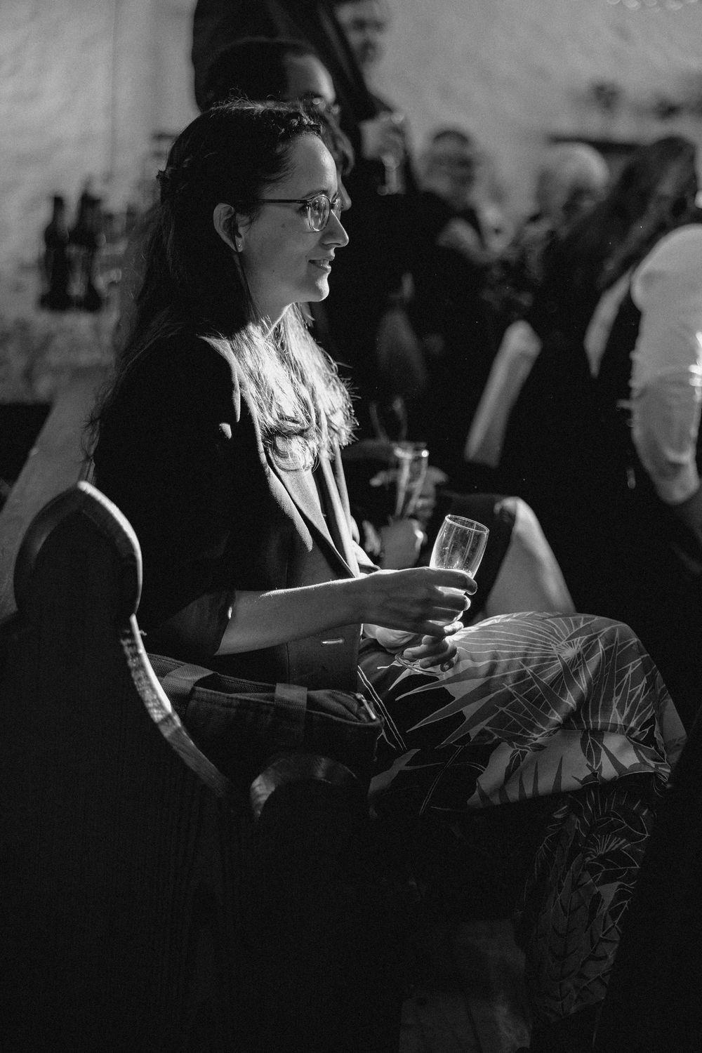 A person in glasses sits holding papers in a black and white candid photograph.
