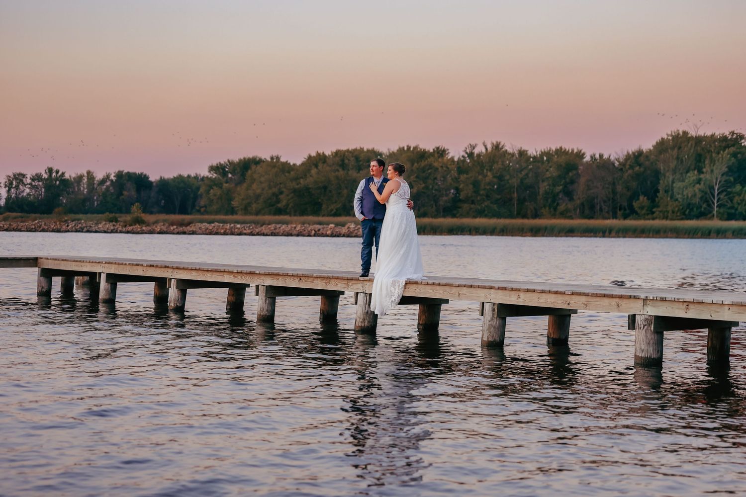 Bride and groom standing together watching the sunset on dock during their wedding portraits in Wisconsin