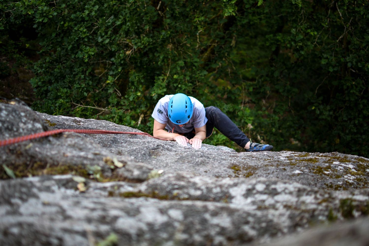 Rock climbers ascending a steep cliff face with climbing gear and ropes in a wooded outdoor setting.