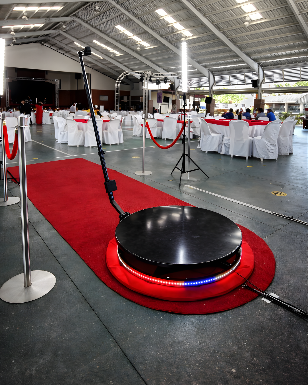 A series of circular black platforms with red carpet surrounds and velvet ropes set up in an industrial event space.