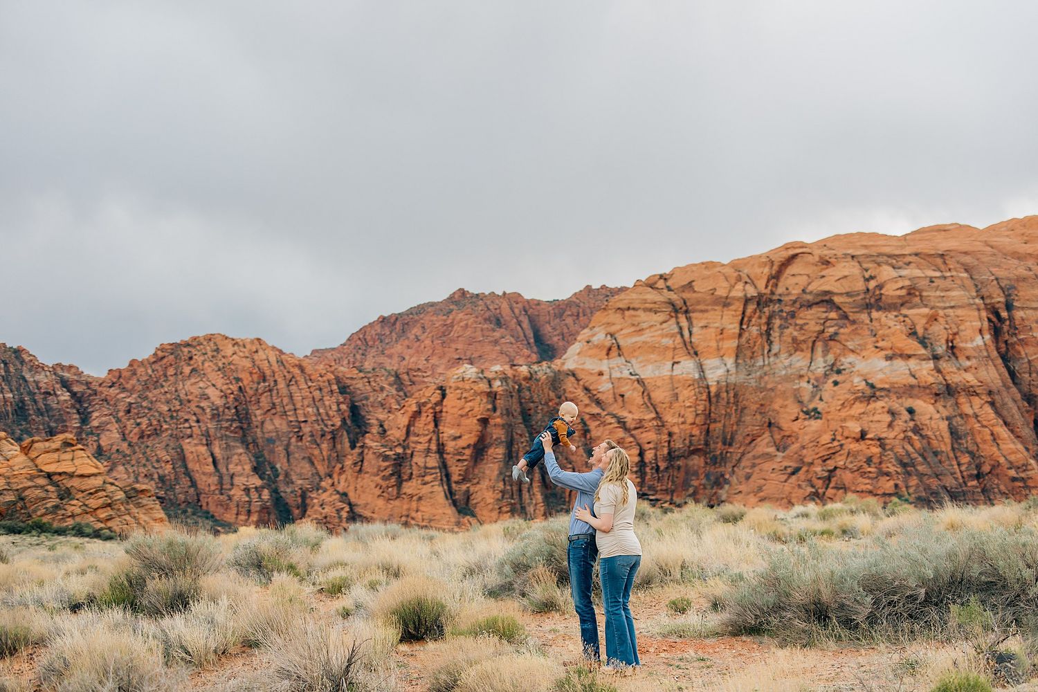 Wide panoramic view of red rock formations and desert landscape with small figures in the distance.