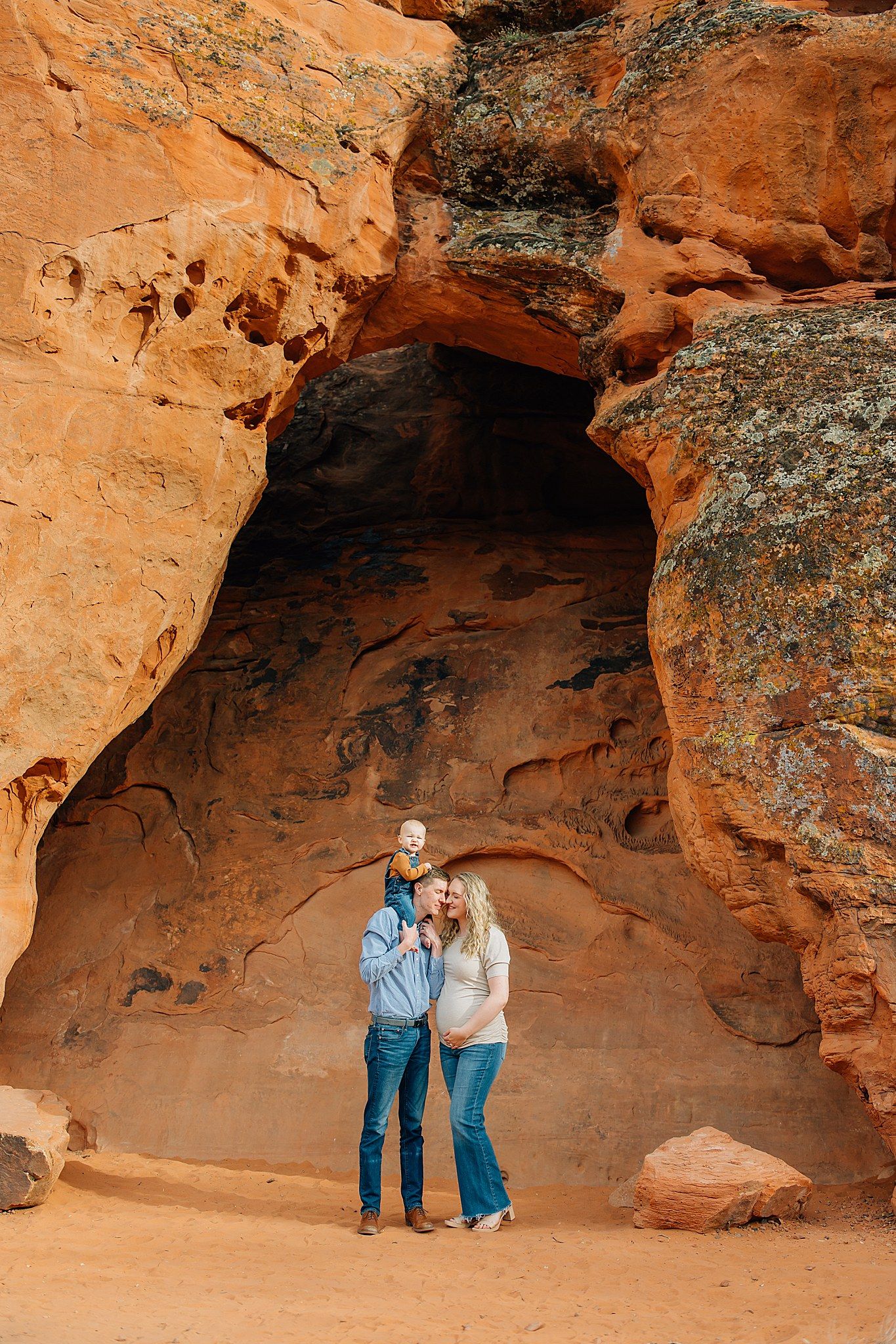 Two people explore a scenic red rock cave formation in a desert landscape during a sunny day.