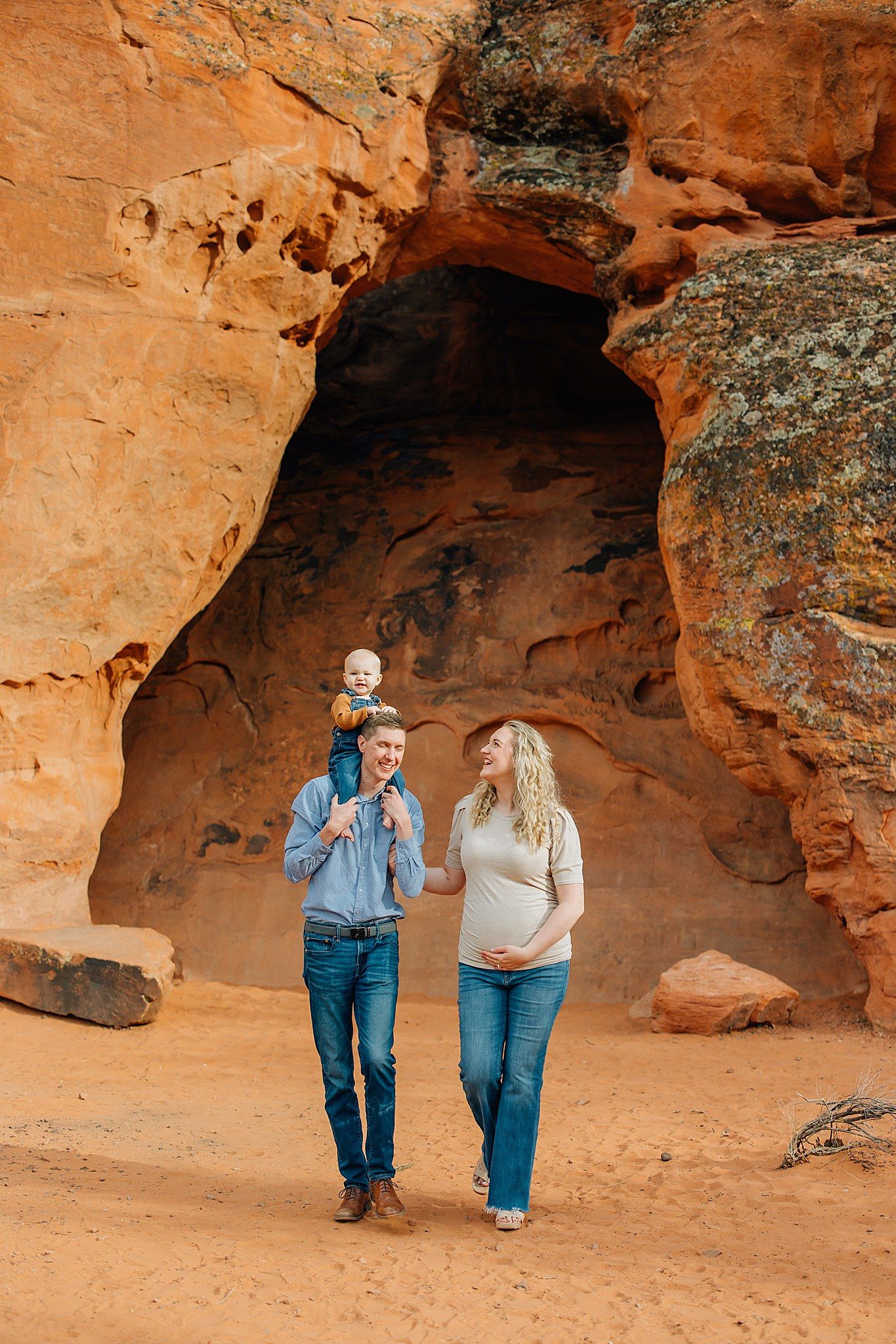 Couple walking through a natural sandstone cave alcove with warm orange walls in the desert.