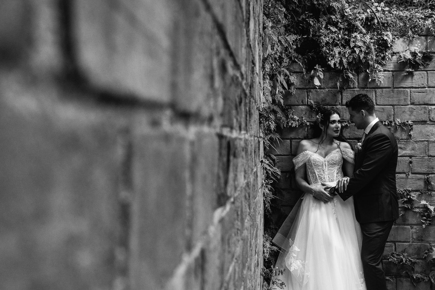 A romantic wedding couple poses in a garden setting with flowing veil and floral bouquet.