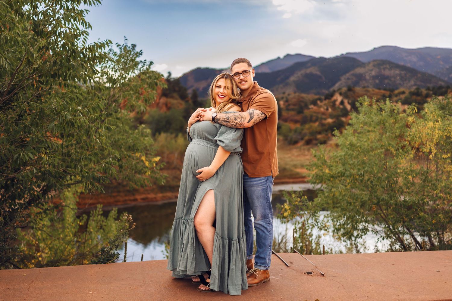 A couple embraces in a scenic outdoor setting with mountains and autumn foliage in the background. Red Rock Canyon, Colorado Springs