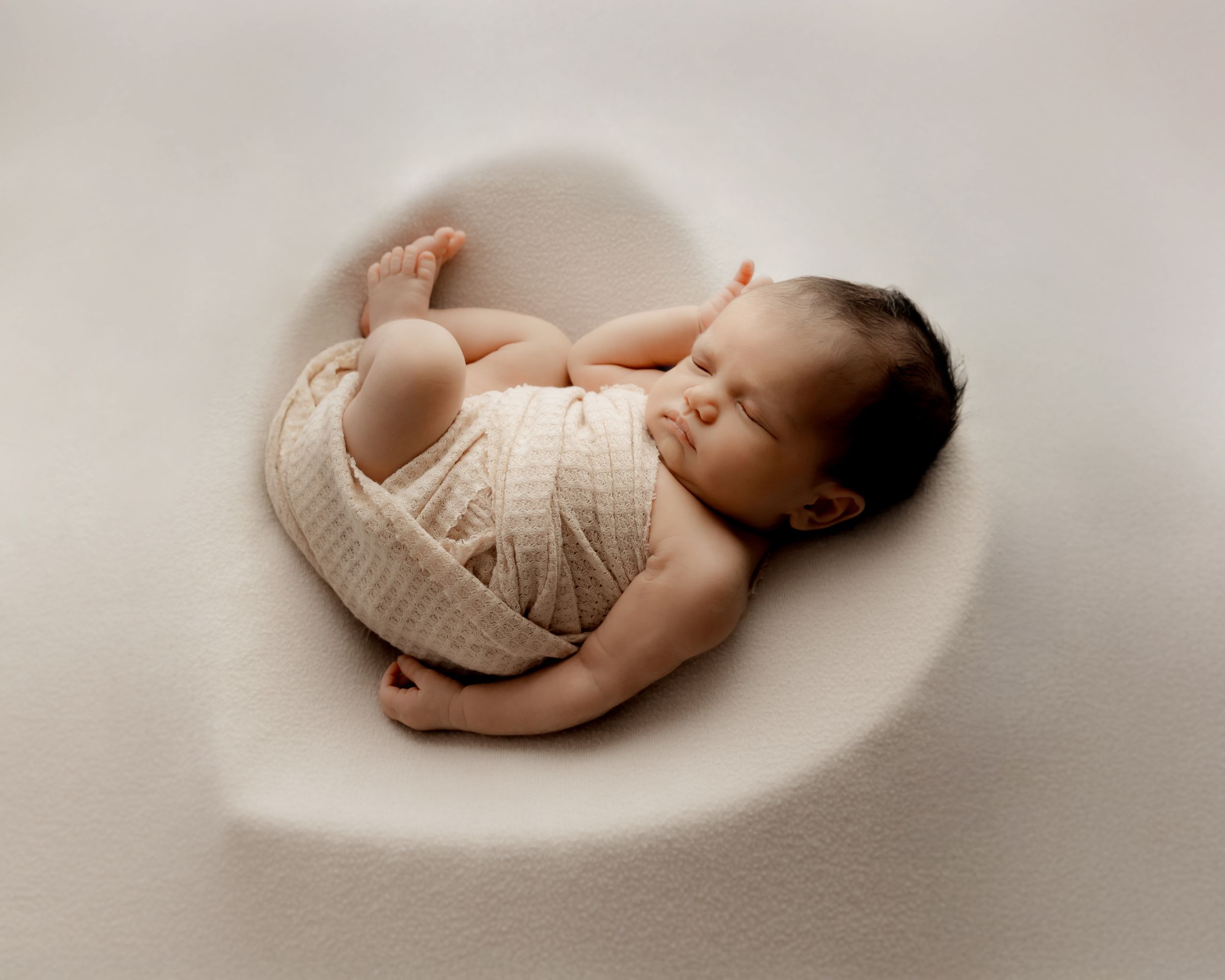 newborn baby sleeping in a heart shape on soft fabric during photo session