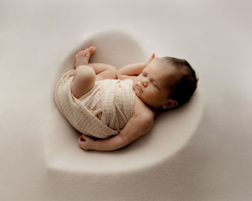 newborn baby sleeping in a heart shape on soft fabric during photo session