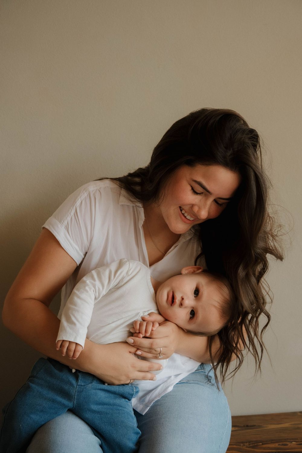 Smiling dark-haired mother in white shirt lovingly holding her baby on her lap.