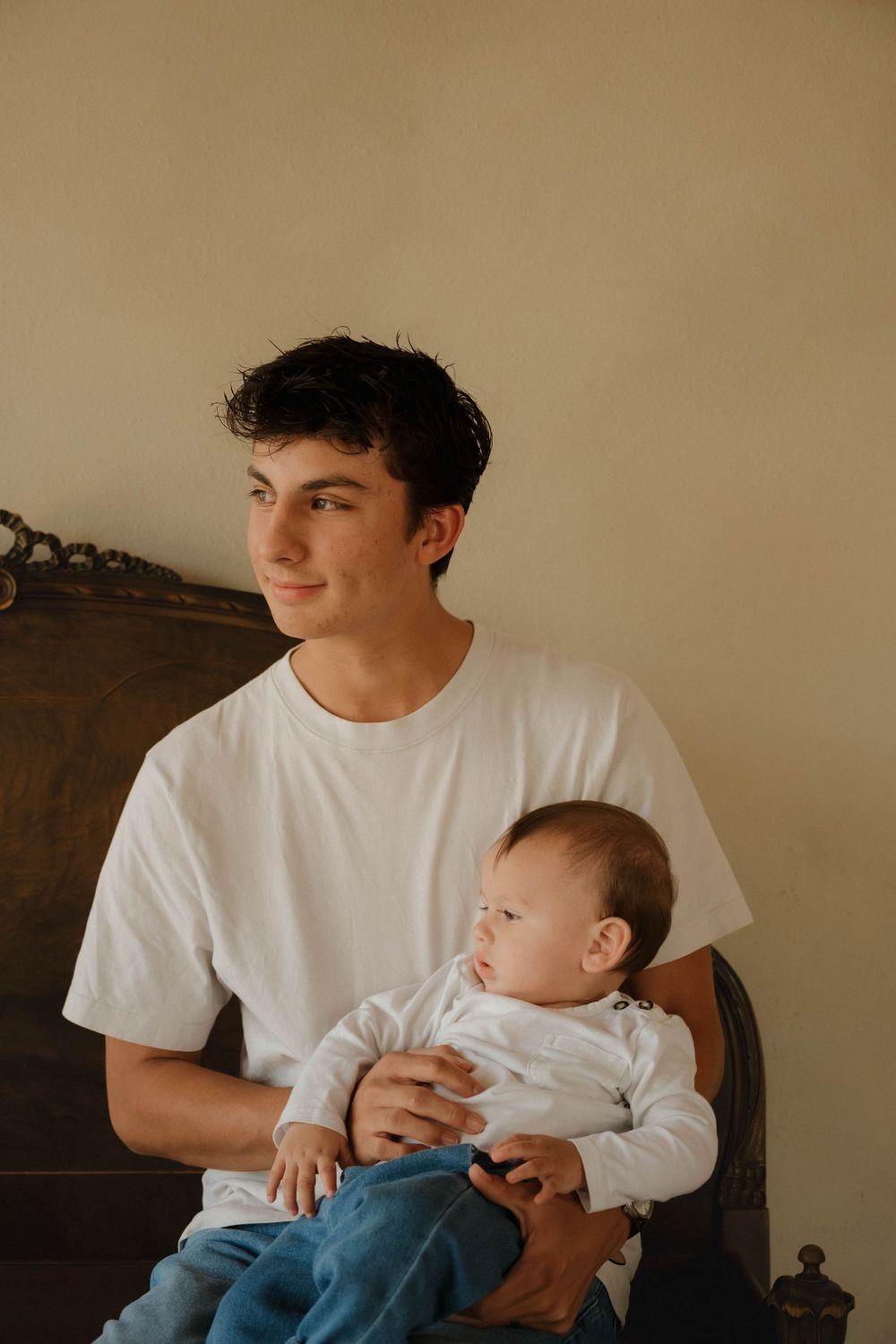 Young man in white t-shirt sitting in chair holding a baby, warm indoor portrait photography.