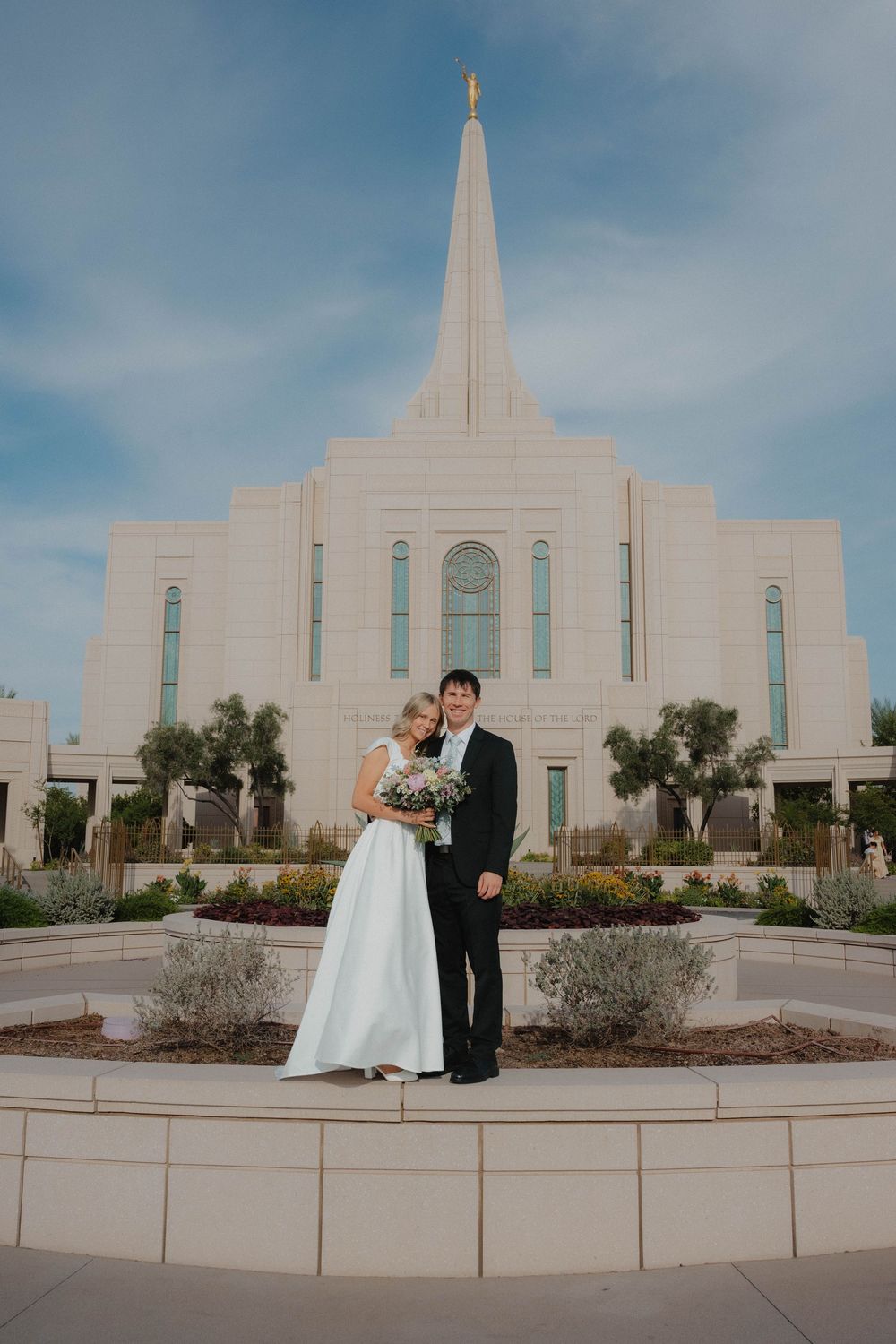 Bride and groom pose together outside the Gilbert Arizona LDS Mormon Temple on their wedding day.