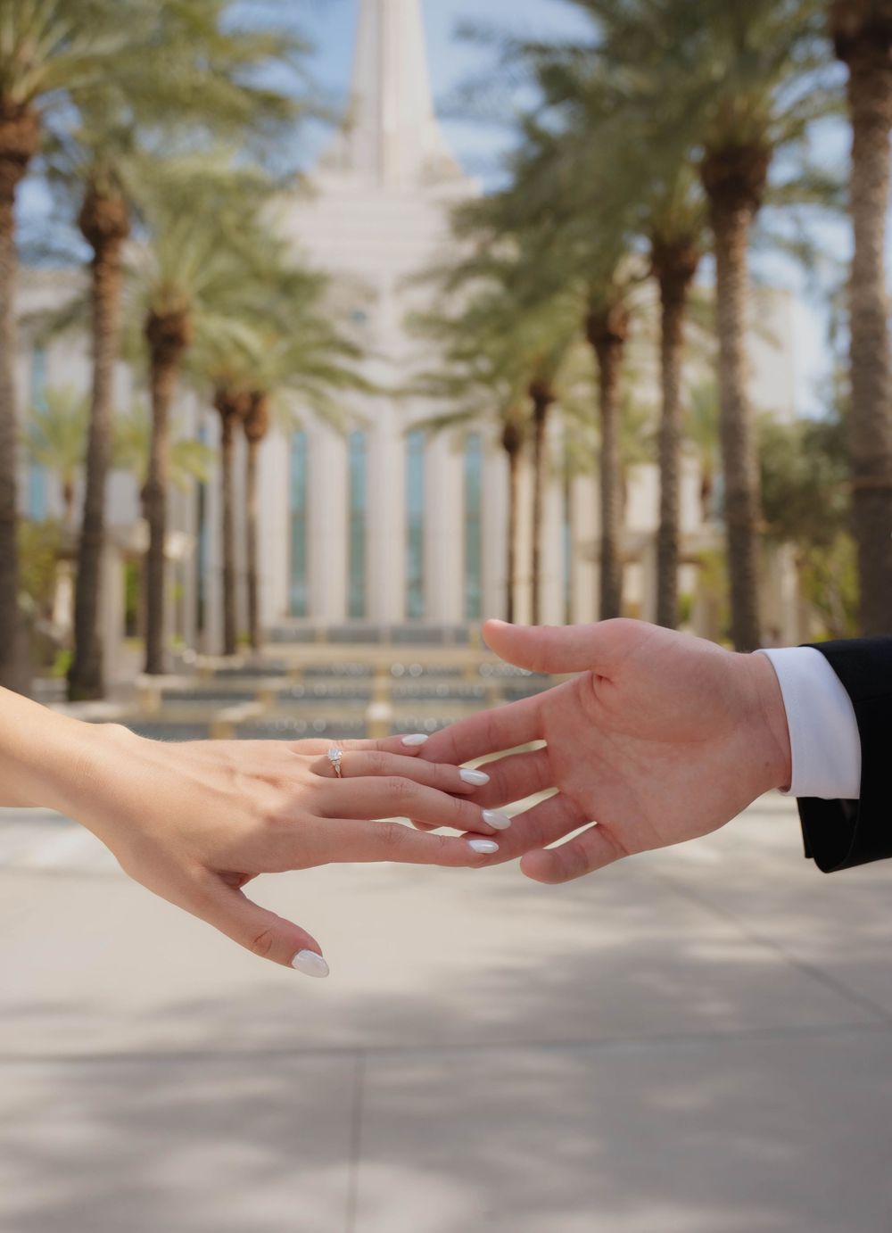 Close-up of bride and groom reaching hands toward each other with wedding rings and temple backdrop.