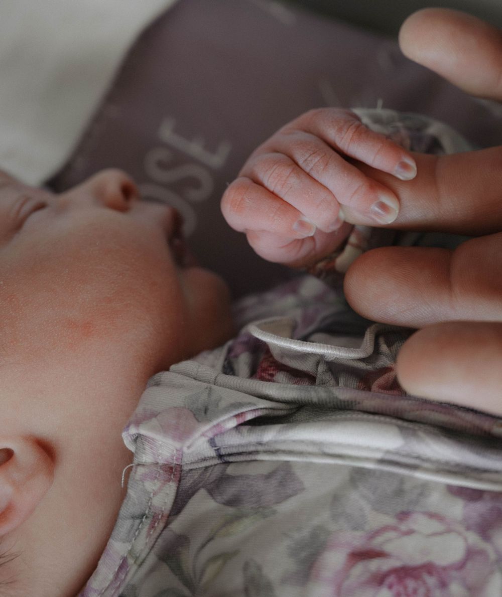 Tender close-up of a newborn baby gently grasping an adult finger while resting peacefully.