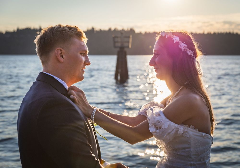 Bride and groom share a tender moment by the water at sunset during their wedding ceremony.