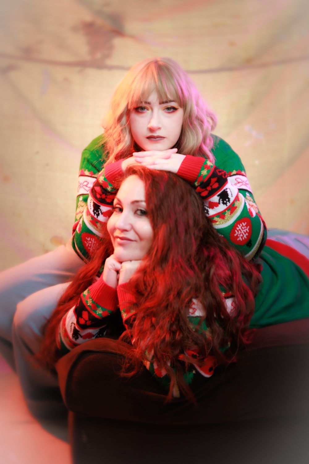 Two women in matching Christmas sweaters pose together, one with blonde hair, one with red hair.
