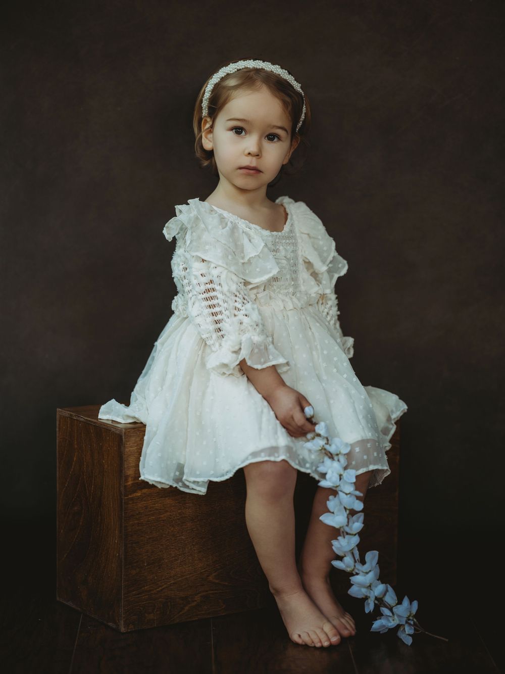 A series of artistic studio portraits showing a child in a vintage-style white lace dress against a dark background.