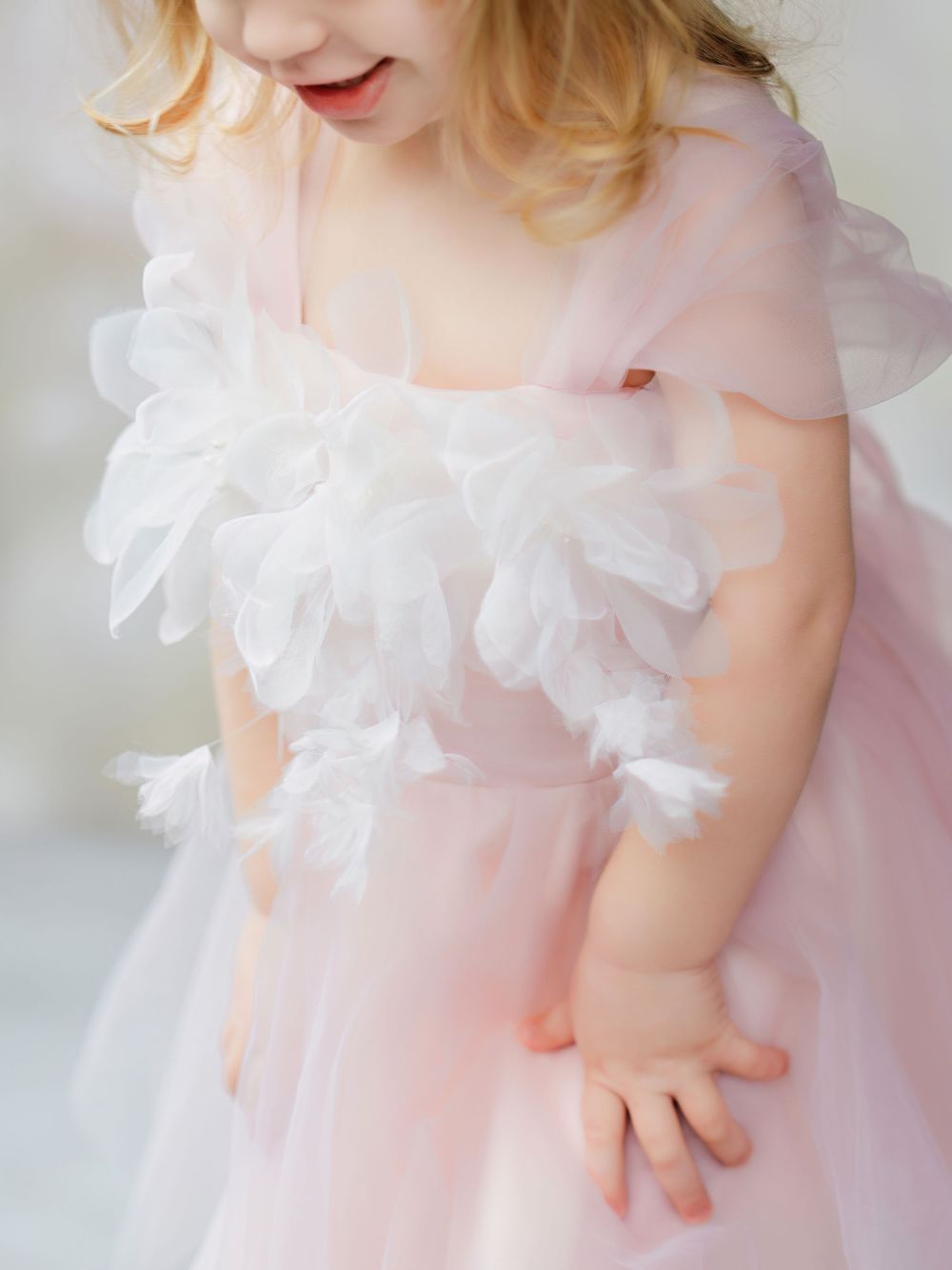 A baby wearing a delicate pink tulle dress with ruffled cap sleeves and soft floral details.