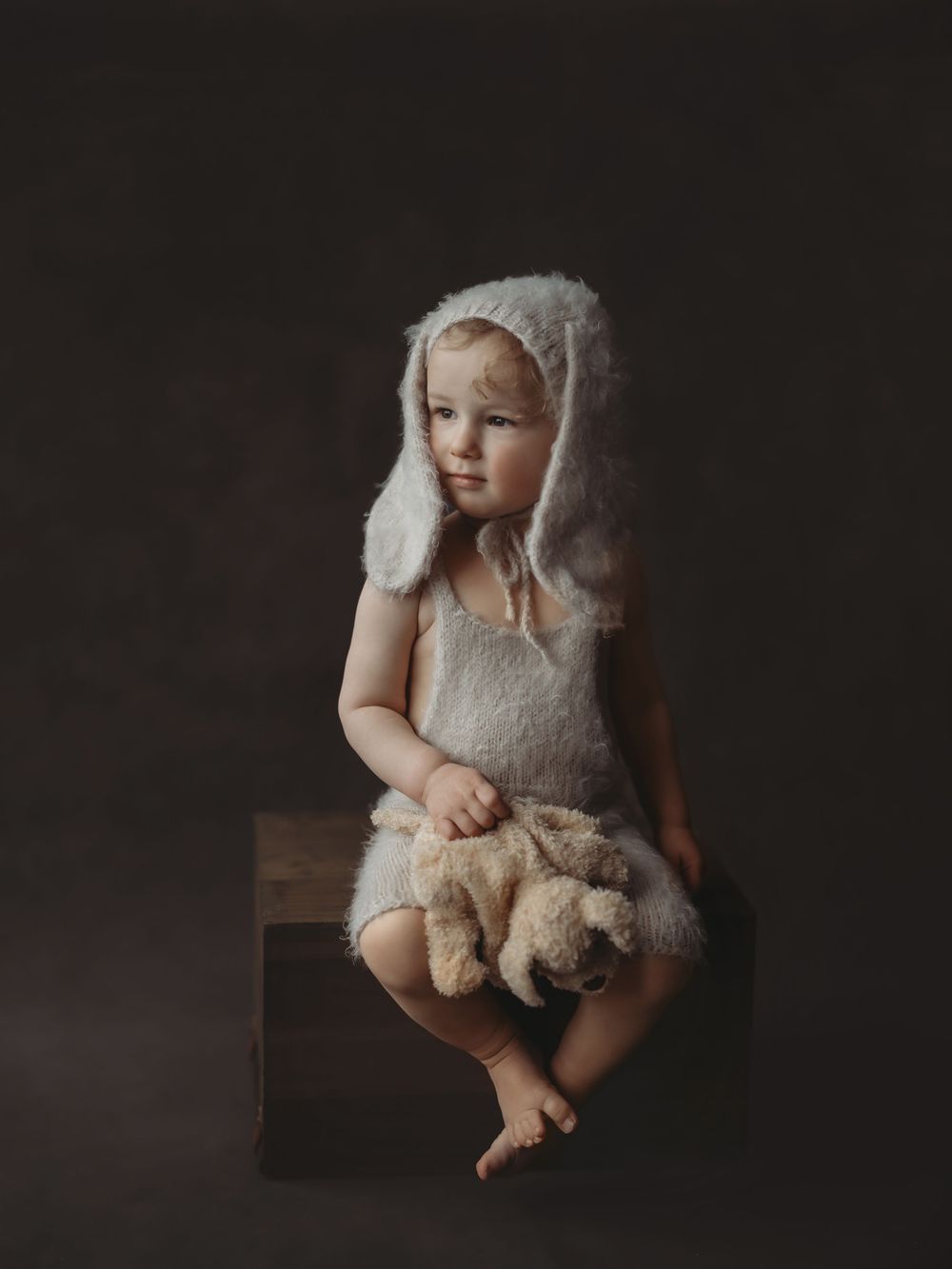 A series of artistic black and white photos showing a baby in a white outfit holding a stuffed animal on a dark background.