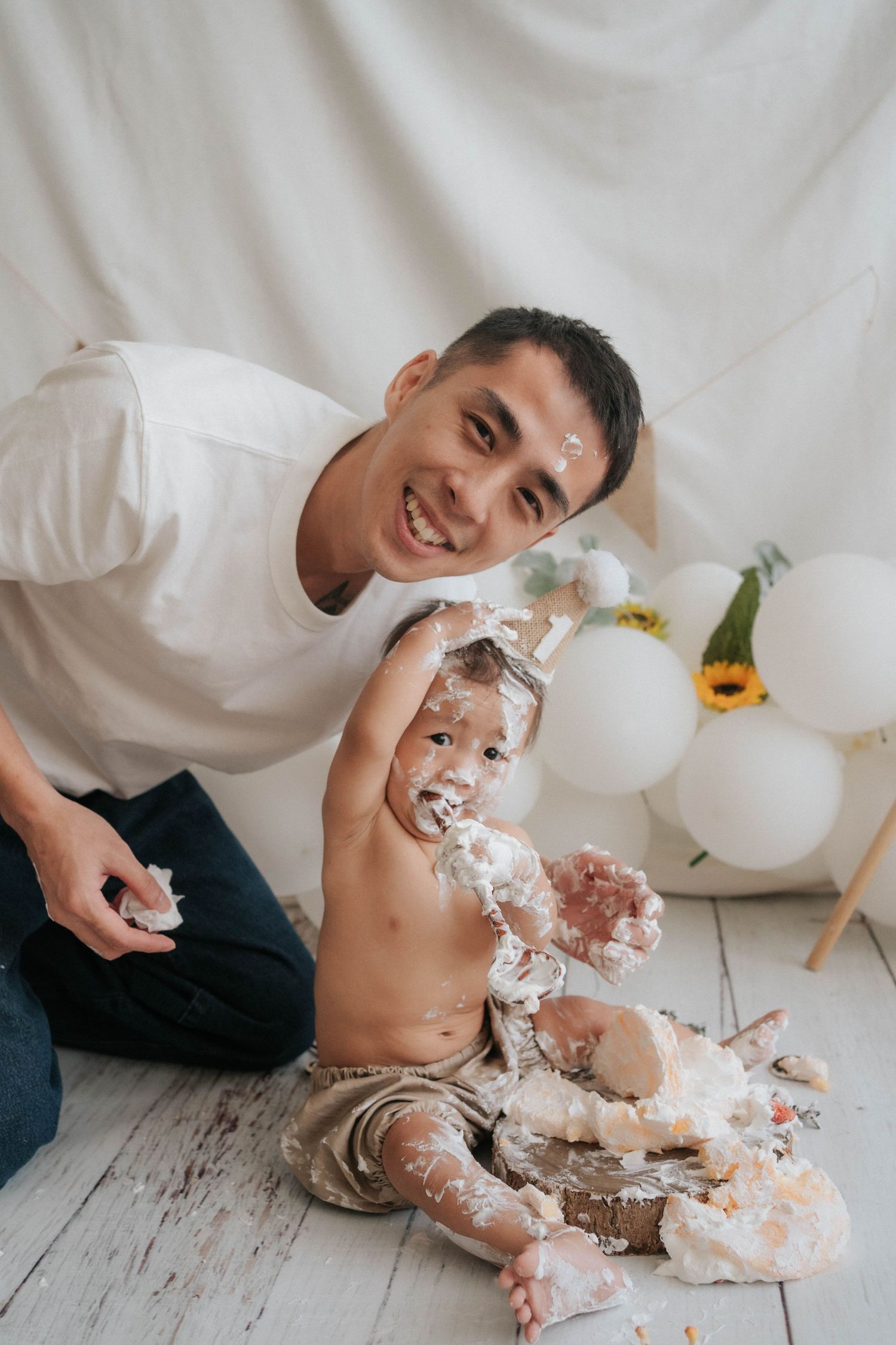 A joyful cake smash photo session showing playful moments with white frosting and decorative flowers on a light backdrop.
