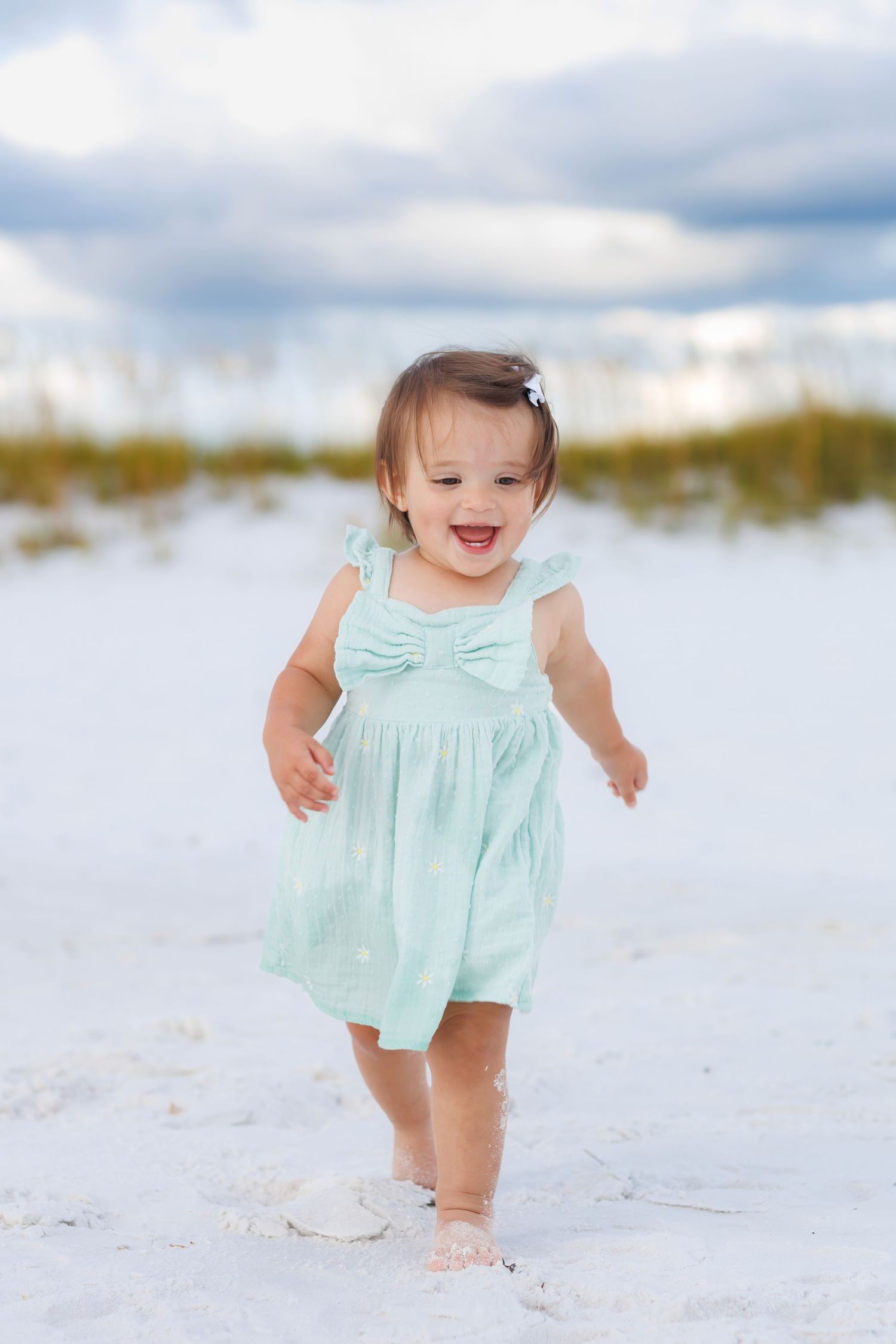 Smiling toddler walking along the shoreline during a natural beach family photography session on the Emerald Coast.
