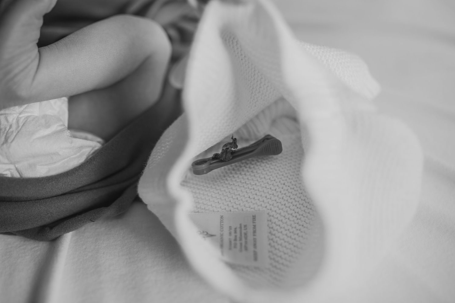 A sleeping baby lies peacefully on white bedding with a small brown teddy bear companion.