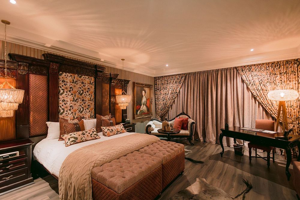 Opulent hotel suite with carved headboard, velvet ottoman, and eclectic vintage decor.
