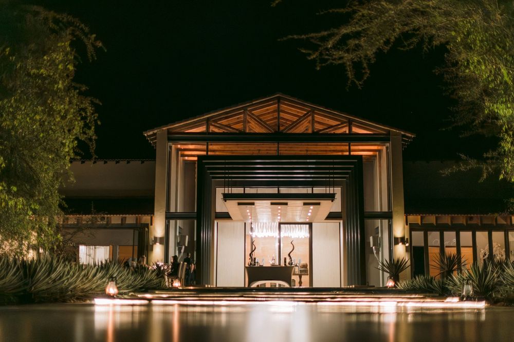 Illuminated luxury lodge entrance at night surrounded by lush trees and warm architectural lighting.