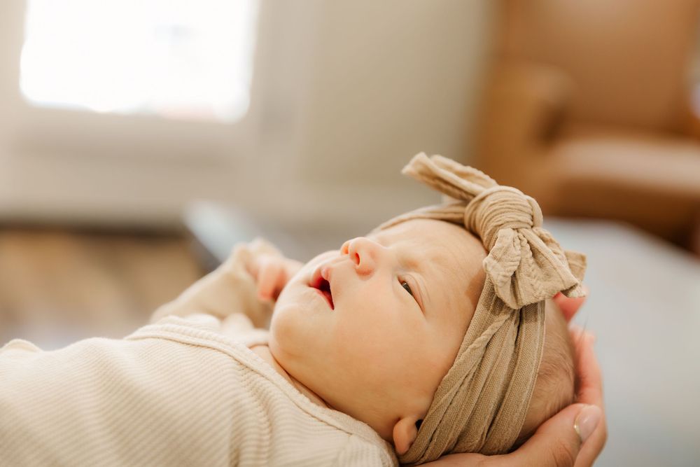 Sleeping newborn baby wrapped in beige swaddle blanket lying on soft white bedding.