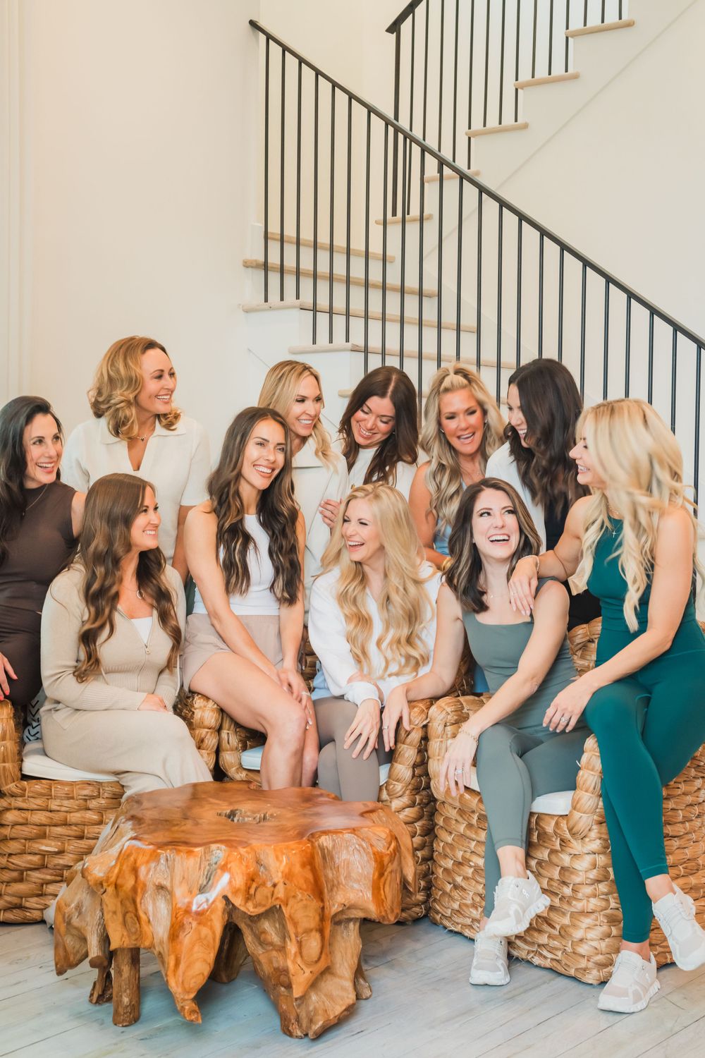 A group of friends sitting and chatting together on woven furniture around a rustic wooden coffee table in a modern home.