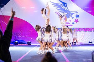 Dancers perform energetic choreography on a brightly lit stage with purple and blue lighting effects.