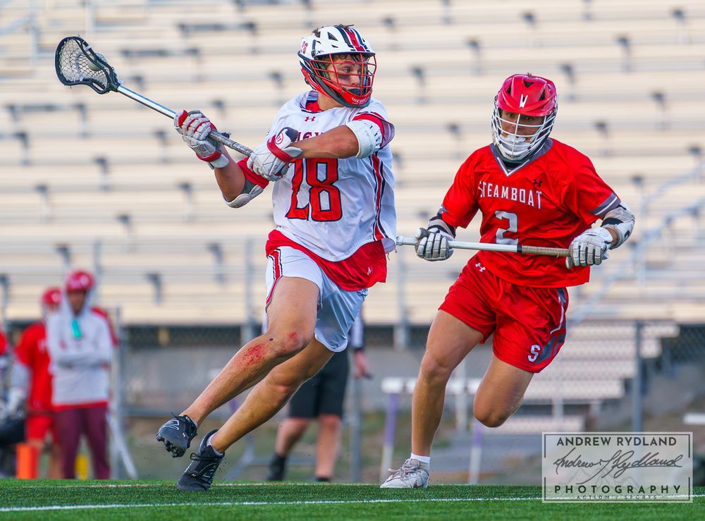 Lacrosse players in red and white uniforms competing during match.