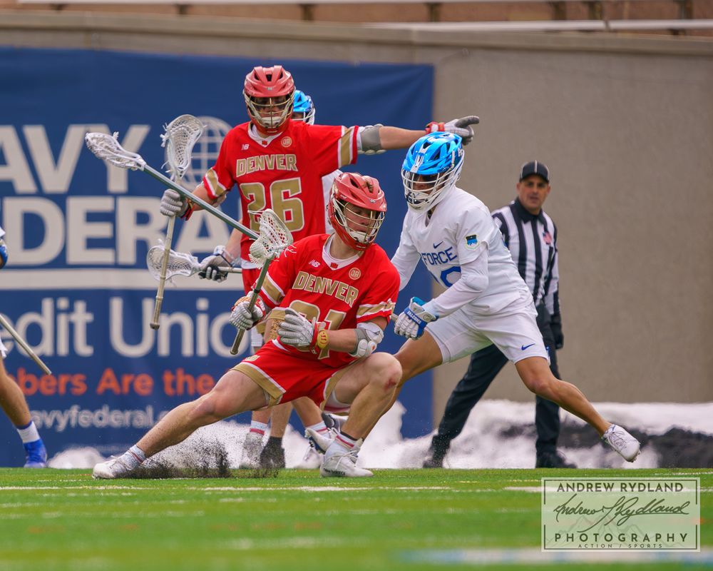 Two lacrosse teams clash in dynamic action with red and white uniforms on stadium field.