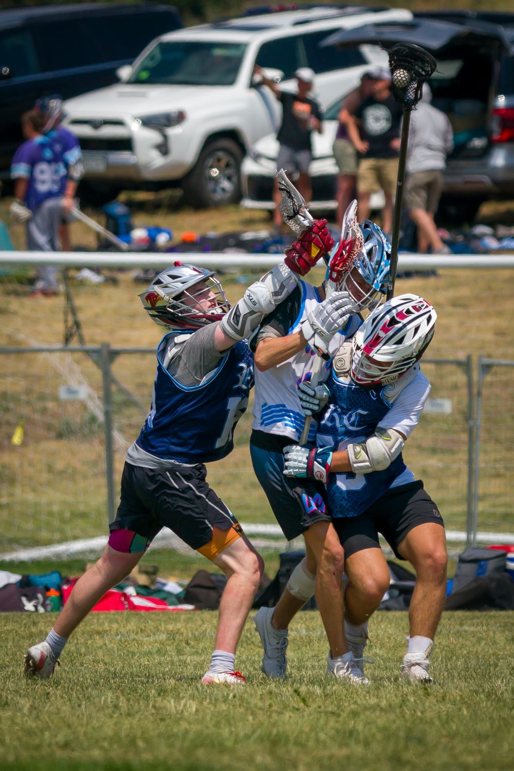 Football players dive and scramble for a loose ball during competitive gameplay on sunny field.