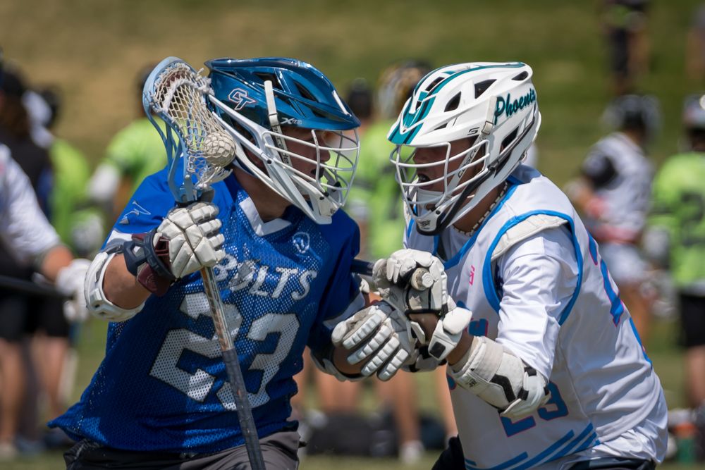 Two lacrosse players in blue and white uniforms engage in close contact during match.