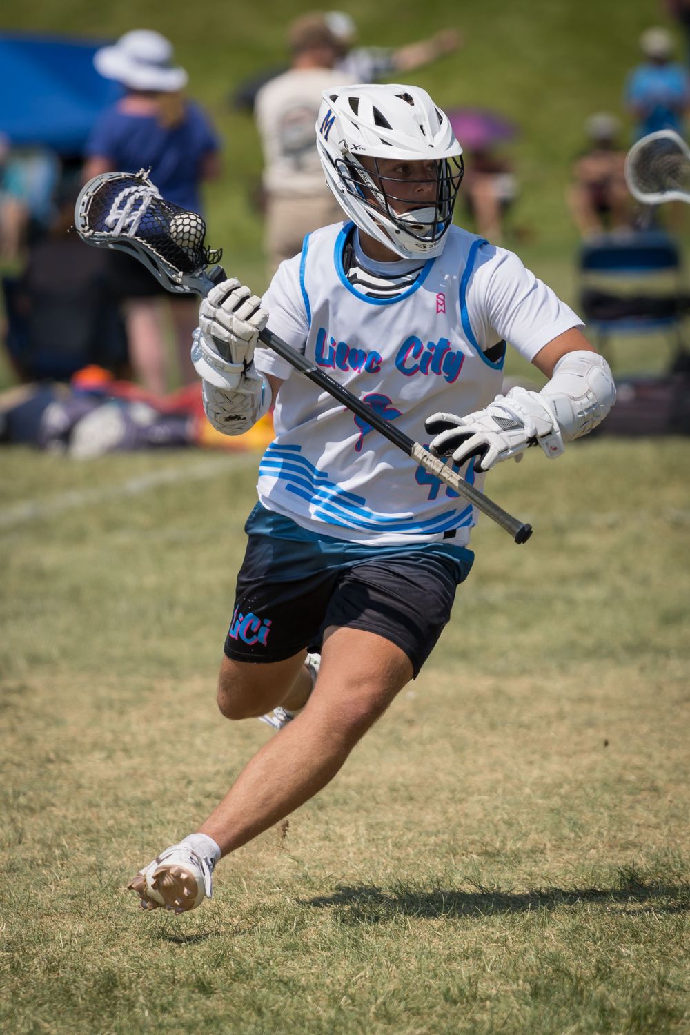 Players in blue and white uniforms lunge for possession during lacrosse match on grass field.