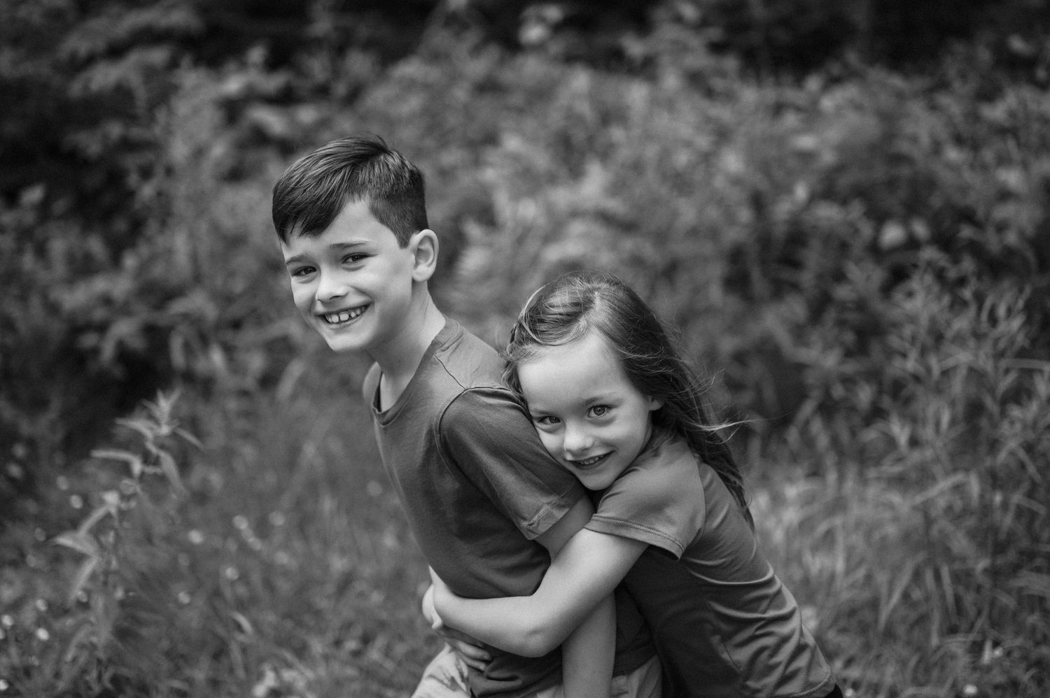 Children playing and embracing outdoors in black and white photography.