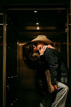 A romantic moment captured in a dimly lit elevator with western style fashion.