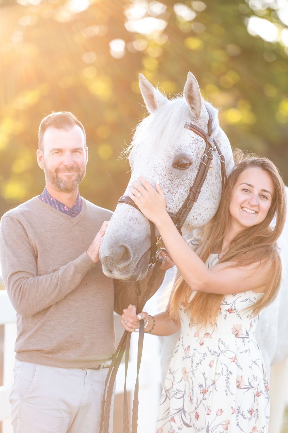 Couple posing with their beautiful white horse during a sunset photoshoot in a romantic outdoor setting.
