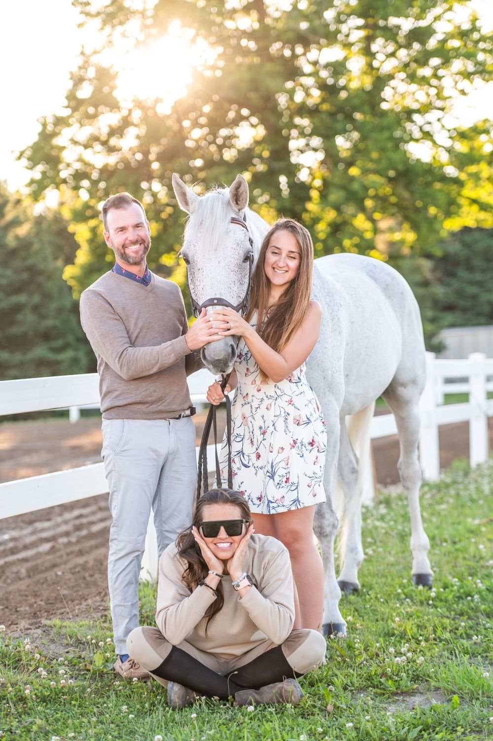 A beautiful white horse poses with its companions at sunset near a white fence, creating a heartwarming outdoor scene.