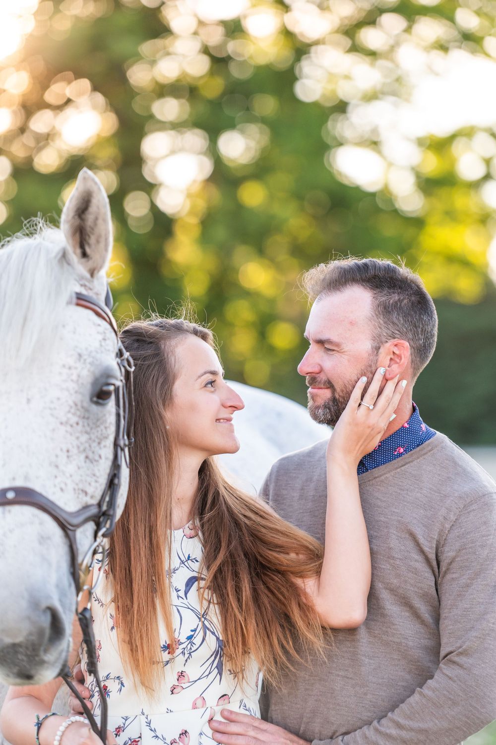 A romantic moment between a couple next to their white horse with dreamy bokeh lighting in the background.