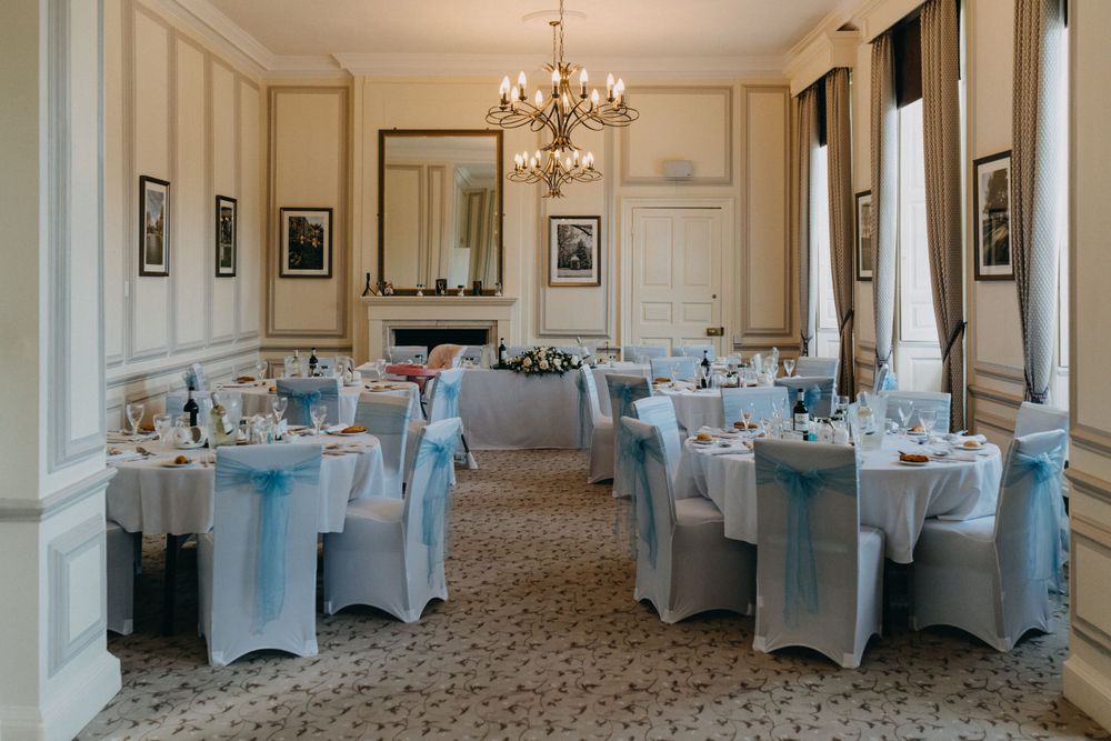 An elegant wedding reception room at Harrowden Hall with crystal chandelier and light blue chair covers.