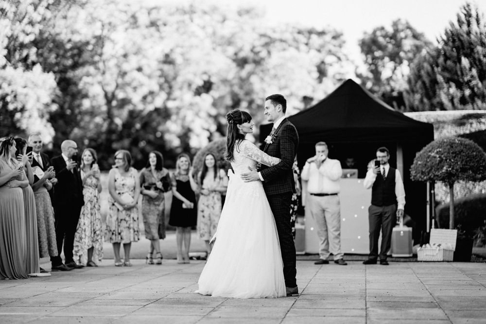 Black and white photo of couple's first dance surrounded by guests at outdoor reception, Harrowden Hall.