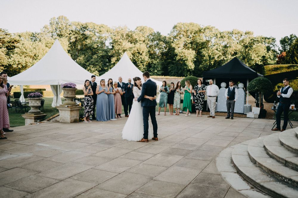 Couple sharing their first dance under outdoor tent with guests looking on.