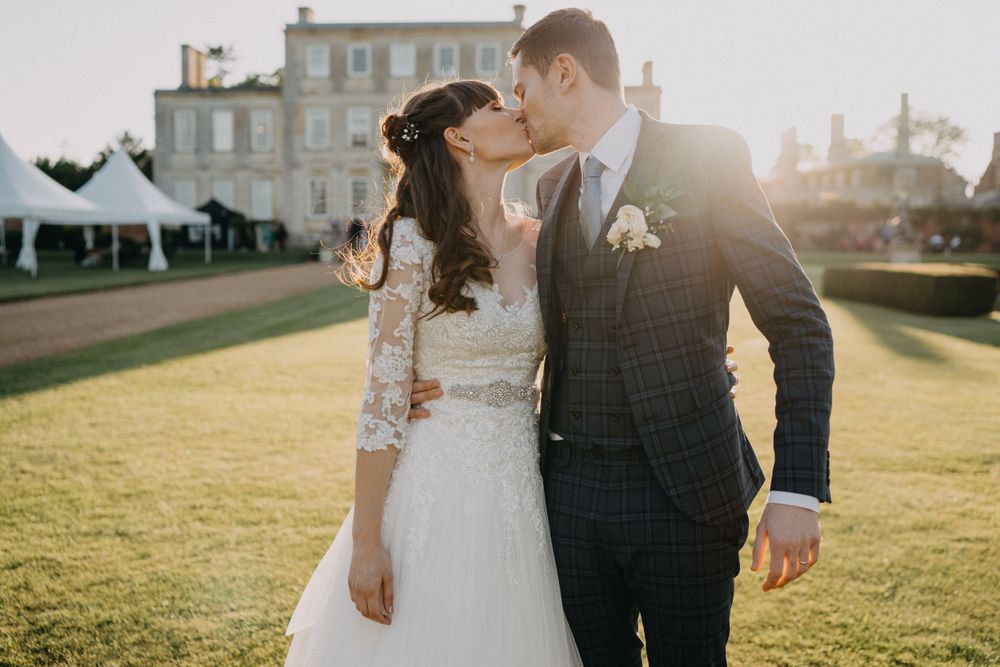 A tender wedding moment captured in golden sunlight with Harrowden Hall in the background.
